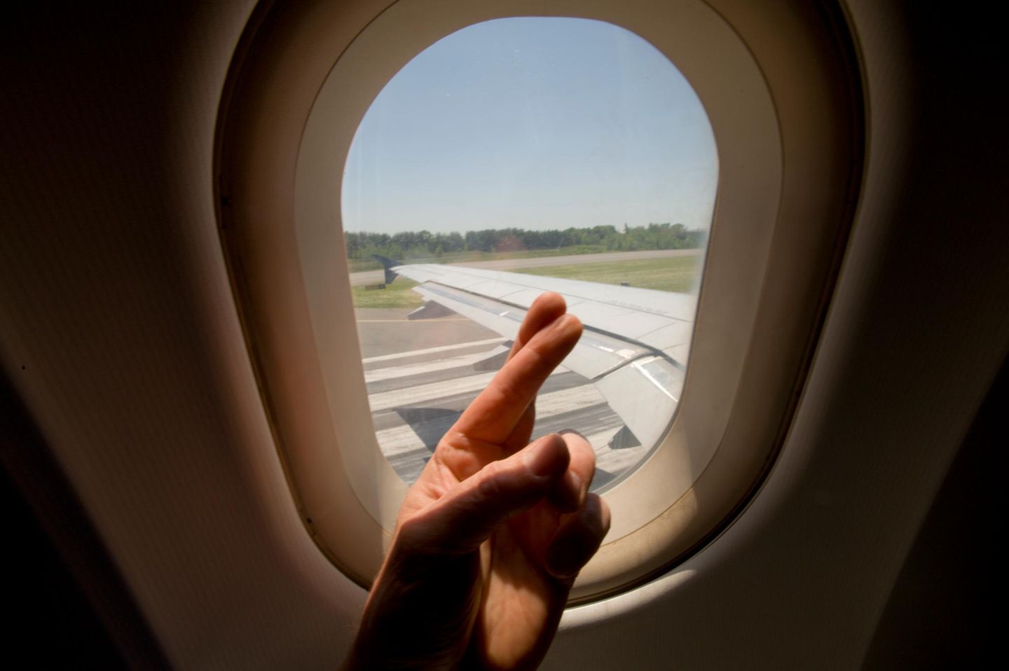 Gekreuzte Finger vor Flugzeugfenster beim Start