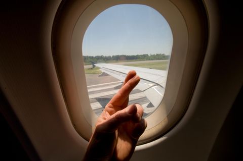 Gekreuzte Finger vor Flugzeugfenster beim Start