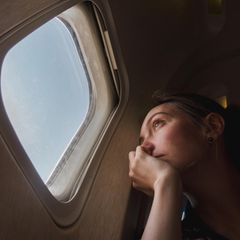 Junge Frau blickt traurig aus einem Flugzeugfenster