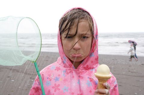 Schlechtgelauntes Mädchen mit Eis im Regen am Strand