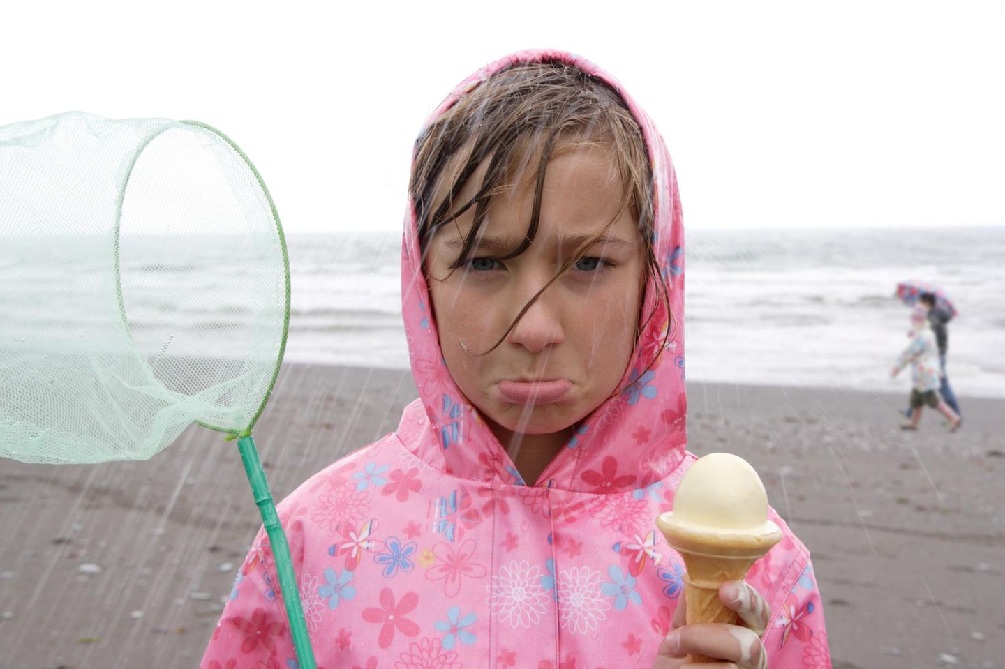 Schlechtgelauntes Mädchen mit Eis im Regen am Strand