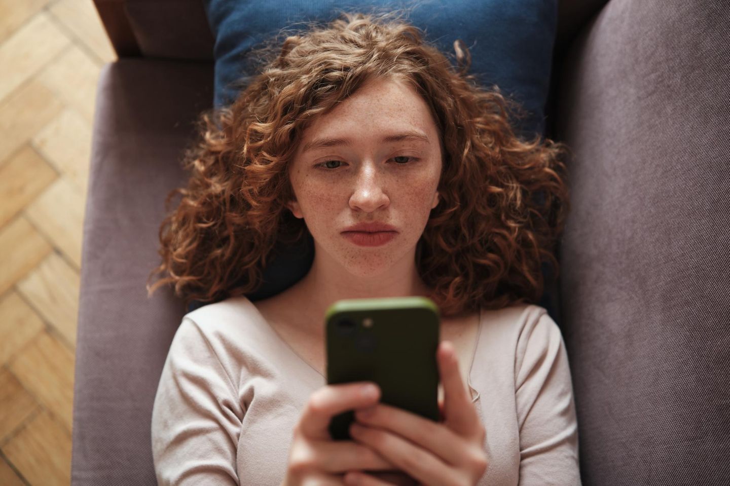 Mädchen mit roten Locken liegt auf dem Sofa und scrollt in ihrem Smartphone