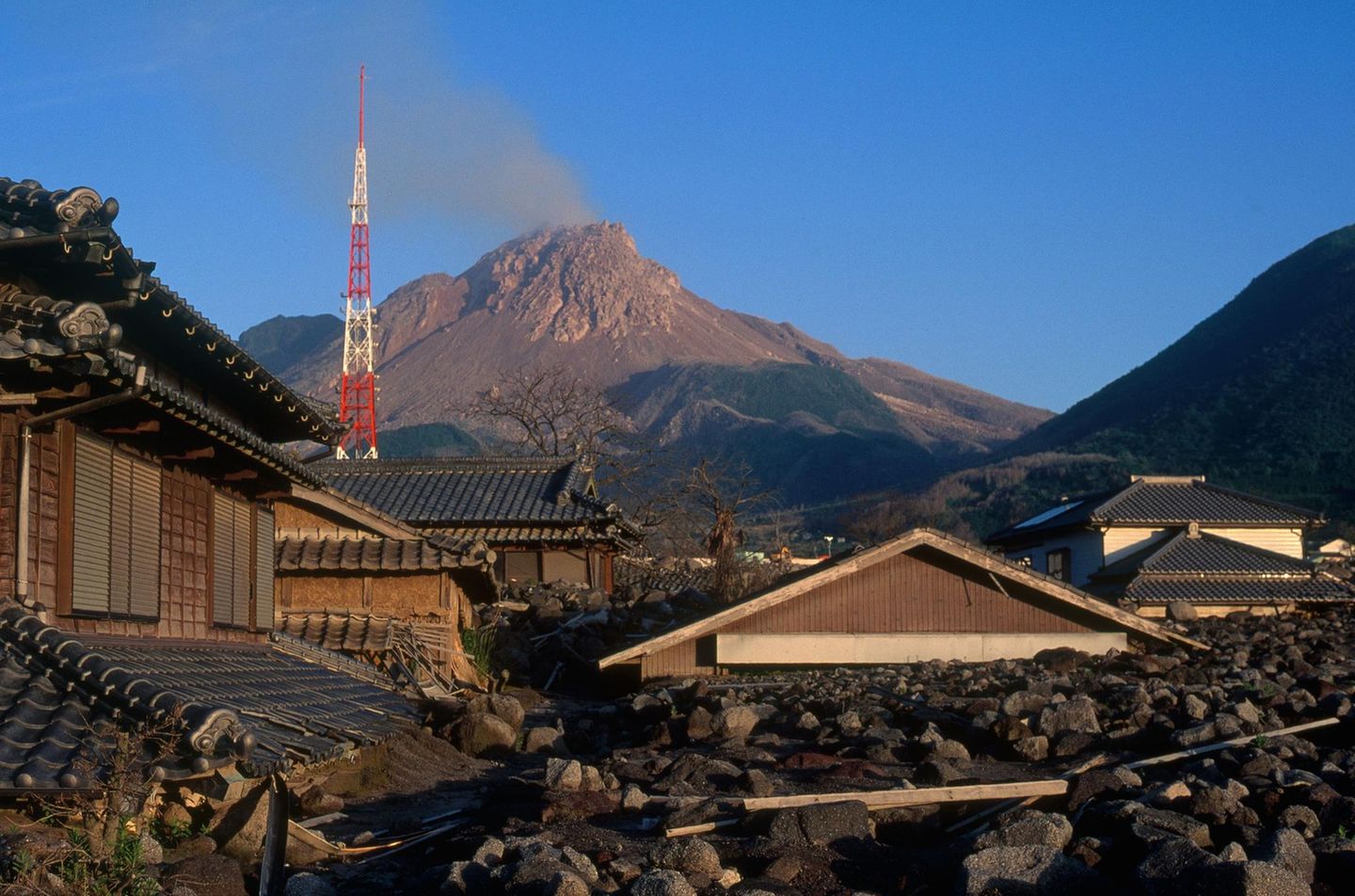 Unzen, Japan Von Geröll und Staub bedeckte Häuser, im Hintergrund der Unzen, aus dem leichter Rauch empor steigt