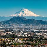 Eine eng besiedelte Stadt mit einem dunklen Berg am Horizont. Dahinter ein schneebedecker noch größerer Berg