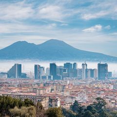 Die Skyline einer Stadt ragt aus Nebel hervor. Im Hintergrund erstreckt sich ein Berg