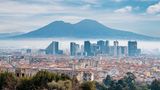 Die Skyline einer Stadt ragt aus Nebel hervor. Im Hintergrund erstreckt sich ein Berg
