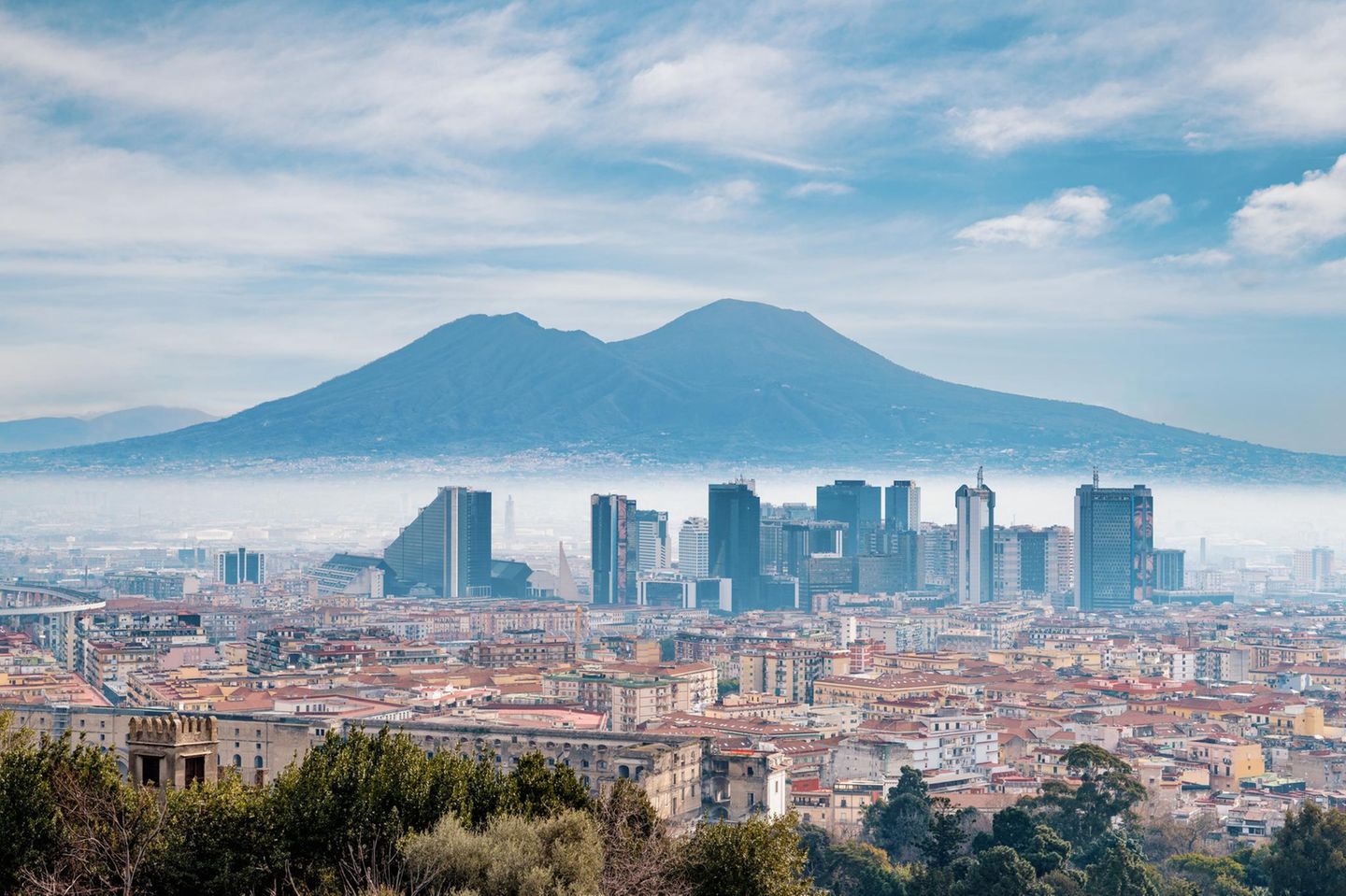 Die Skyline einer Stadt ragt aus Nebel hervor. Im Hintergrund erstreckt sich ein Berg