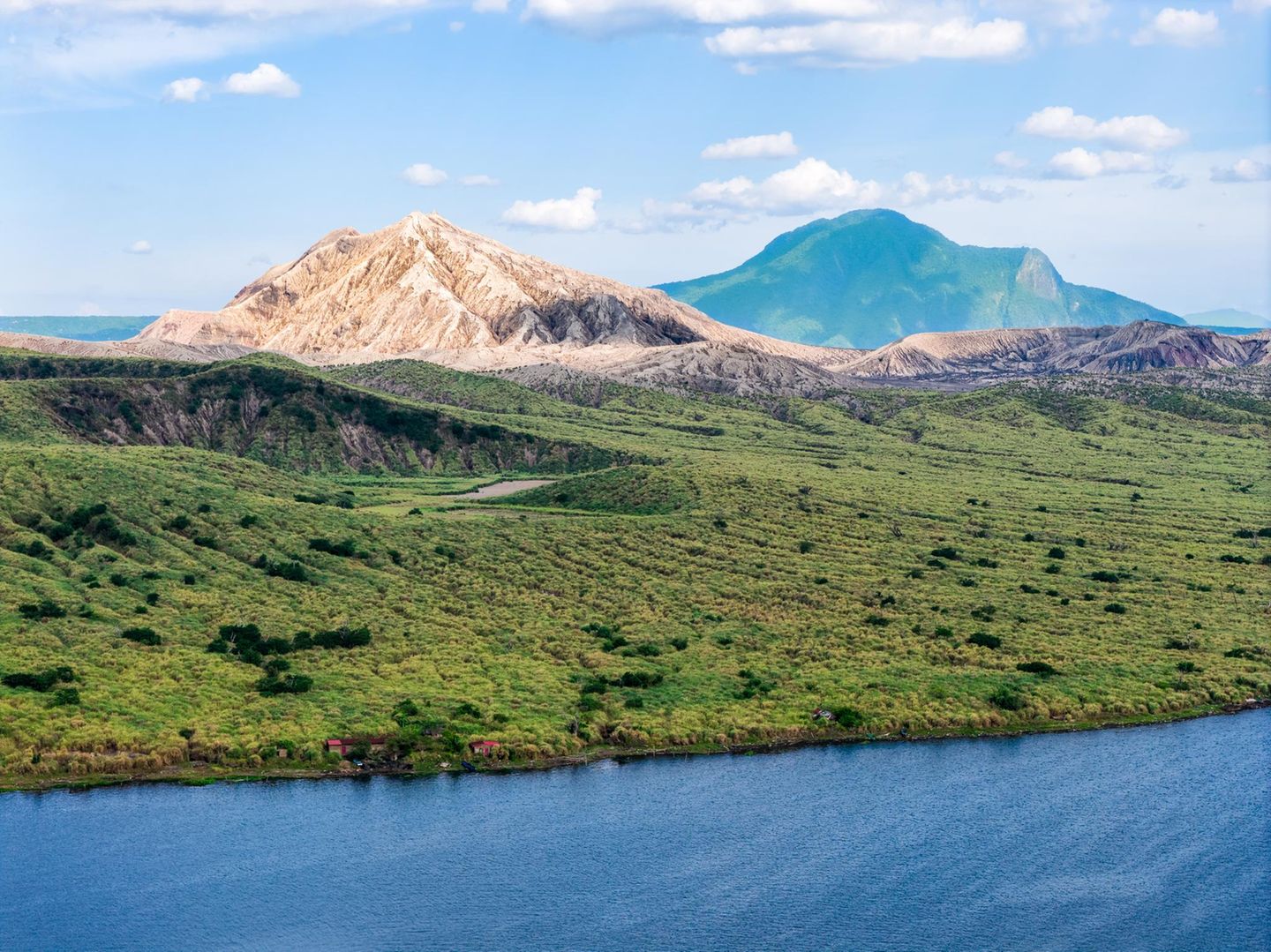 Hinter einer grünen Wiese ragt der Taal-Vulkan empor