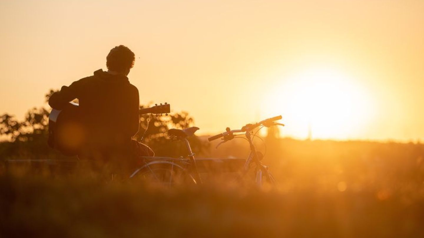 Mann spielt bei Sonnenuntergang Gitarre in der Natur. Neben ihm steht ein Fahrrad