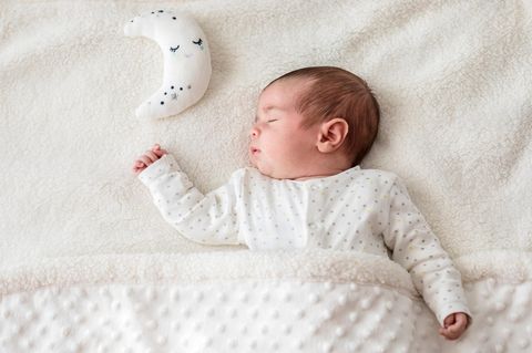 Neugeborenes liegt mit geschlossenen Augen neben einem weißen mondförmigen Kuscheltier