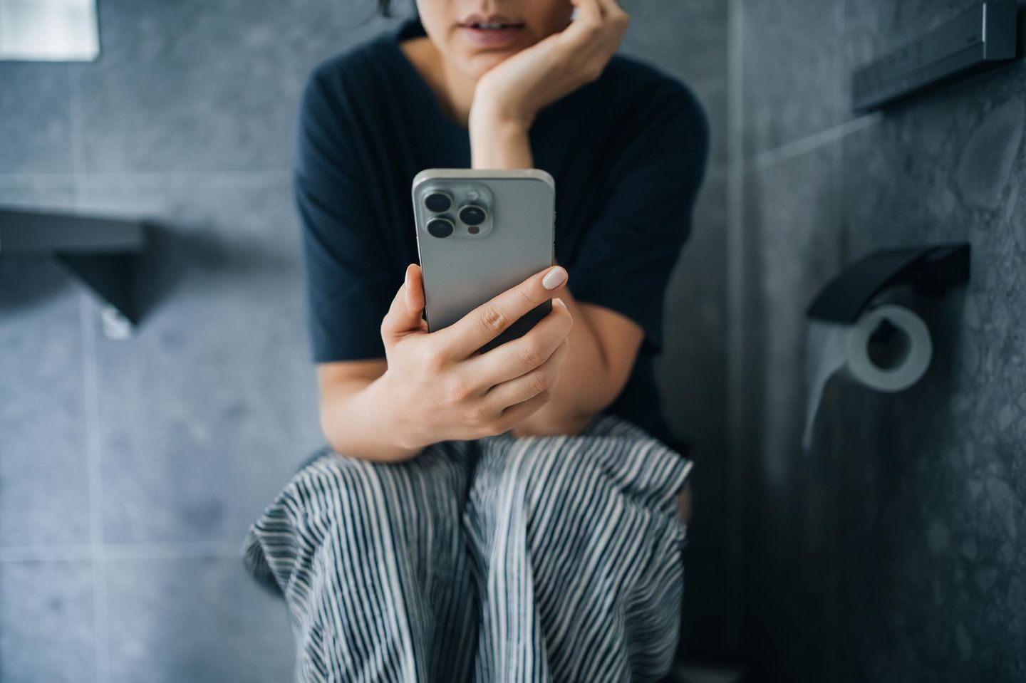 Person sitzt mit einem Smartphone in der Hand auf der Toilette