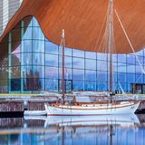 Glasfassade und Eichenholzdach des Kilden Theater- und Konzerthauses, davor Schiff im Wasser