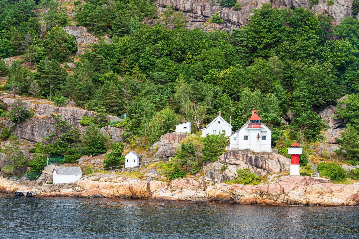 Blick auf den Leuchtturm Odderøya Fyr, dahinter Felsen und Bäume