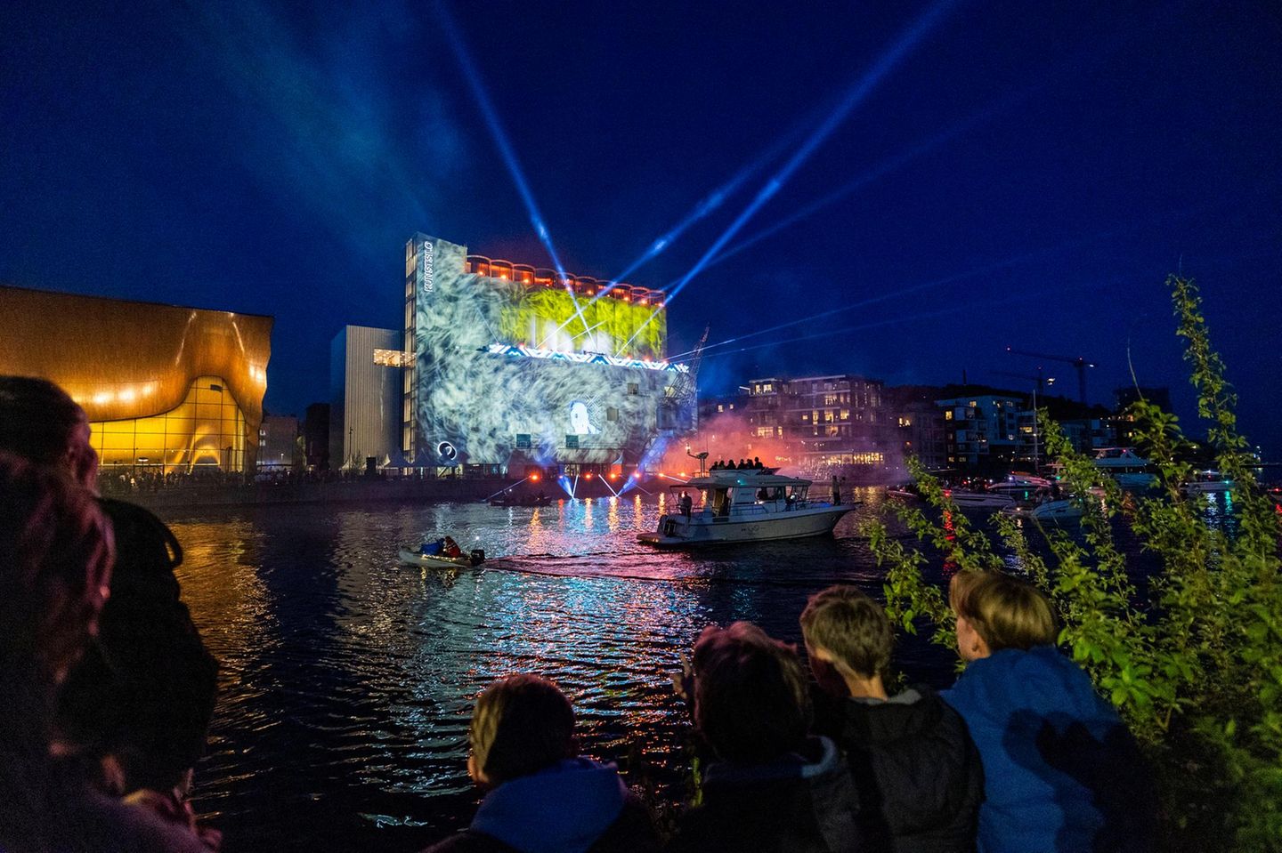 Moderne Kunst im Spotlight: Museum und Kulturzentrum Kunstsilo Bunt beleuchtetes "Kunstsilo" in Kristiansand, davor Wasser und Menschen