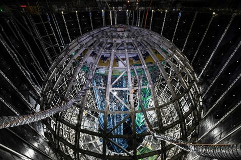 Geisterteilchen. Neutrinos sind die leichtesten und zugleich am schwersten detektierbaren Teilchen des Kosmos. In jeder Sekunde fliegen Zigmilliarden durch einen menschlichen Körper, ohne dass wir es bemerken. Diese 35 Meter hohe kugelförmige Stahlkonstruktion, von chinesischen Forschenden kürzlich fertiggestellt, soll sie aufspüren und ihnen ihre Geheimnisse entlocken.   Umgeben mit einem Panzer aus Plexiglas fasst die Kugel 20.000 Tonnen einer Flüssigkeit, die aufleuchtet, wenn Neutrinos sie durchqueren. Um dem Innendruck der Flüssigkeit auf die Außenfläche etwas entgegenzusetzen, schwebt die Kugel in einem riesigen Wasserbecken, 44 Meter tief, angefüllt mit 60.000 Tonnen hochreinem Wasser. Und als wäre das nicht schon megalomanisch genug, befindet sich die gesamte Konstruktion 700 Meter unter der Erde, um sie vor äußeren Störungen zu schützen.   Solch ein Aufwand wäre wohl übertrieben, wäre das Neutrino nicht das mysteriöseste und am wenigsten verstandene Elementarteilchen. Forschende können viele seiner Eigenschaften nicht erklären: Es besitzt eine (winzige) Masse, auch wenn es das nicht sollte; es kann sich nur in eine Richtung drehen und ein einzelnes wandelt sich unentwegt in verschiedene Arten von Neutrinos um. Mit der Kugel wollen Forschende dieses ungewöhnliche Verhalten genauer beobachten und verstehen, in der Erwartung und Hoffnung, etwas fundamental Neues über das Universum zu lernen.  KW 36