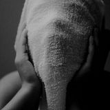 Ein Kind hält sich ein Handtuch vor das Gesicht und hält es mit den Händen. Der Mund ist weit offen