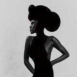 Eine Person ist gekleidet in einem schwarzen Kleid und trägt einen runden schwarzen Hut. Sie macht eine elegante Pose