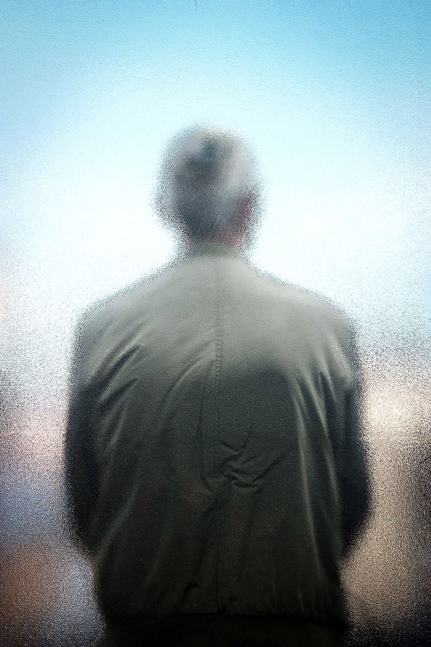 Eine Person von hinten, die mit dem Rücken an einer Scheibe lehnt