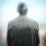 Eine Person von hinten, die mit dem Rücken an einer Scheibe lehnt