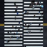 Ein Zebrastreifen von oben mit vielen Menschen, die die Straße überqueren