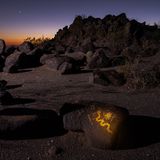 In einer Landschaft leuchtet ein mit gelber Farbe bemalter Stein auf, welcher das Symbol einer Schlange zeigt