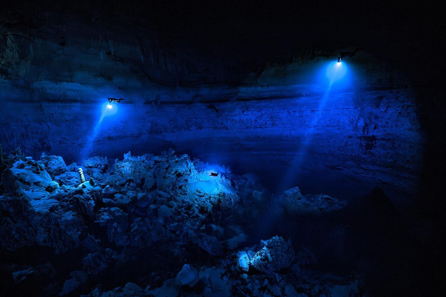 Taucher in der Yab Yum Höhle, welche sich in der Dunkelheit mit ihren blauen Lampen von der Umgebung abheben