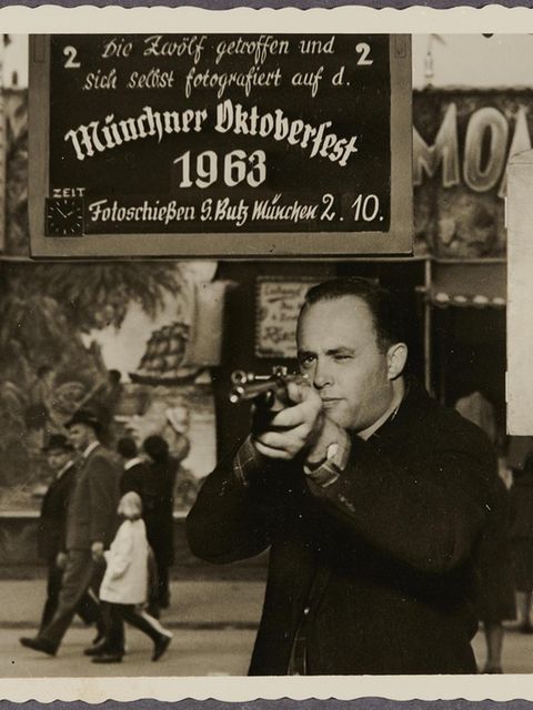 Ein Mann zielt mit einem Gewehr, im Hintergrund ein Schild