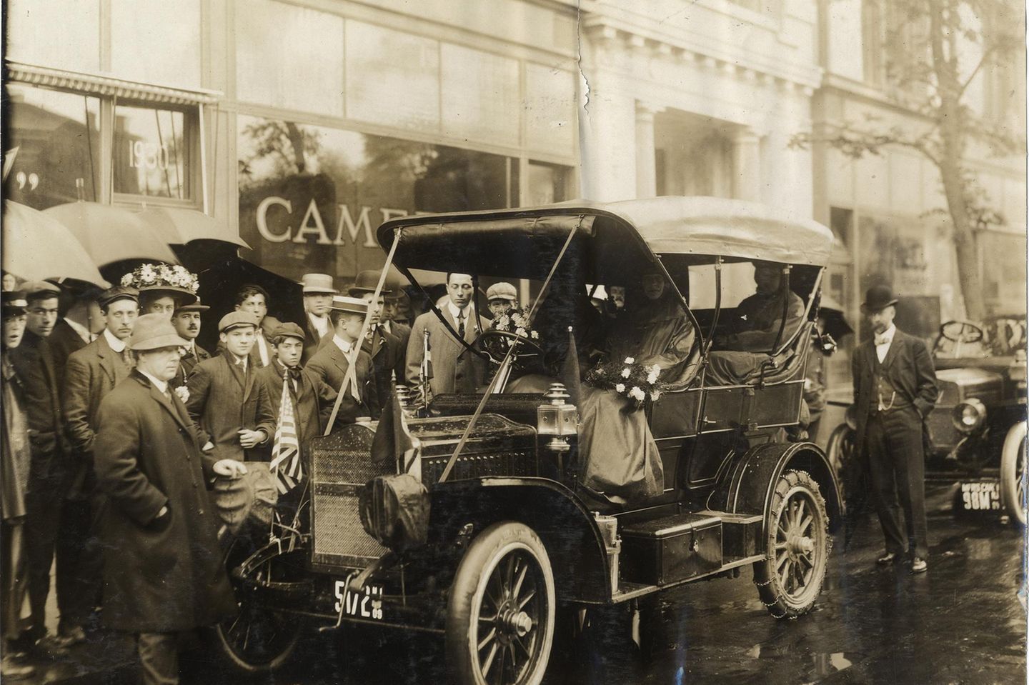 Eine Menschentraube mit Regenschirmen steht zwischen einem Auto und Gebäuden in New York