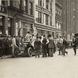 Eine Menschentraube vor einem parkenden Auto, in dem eine Frau steht und nach hinten schaut