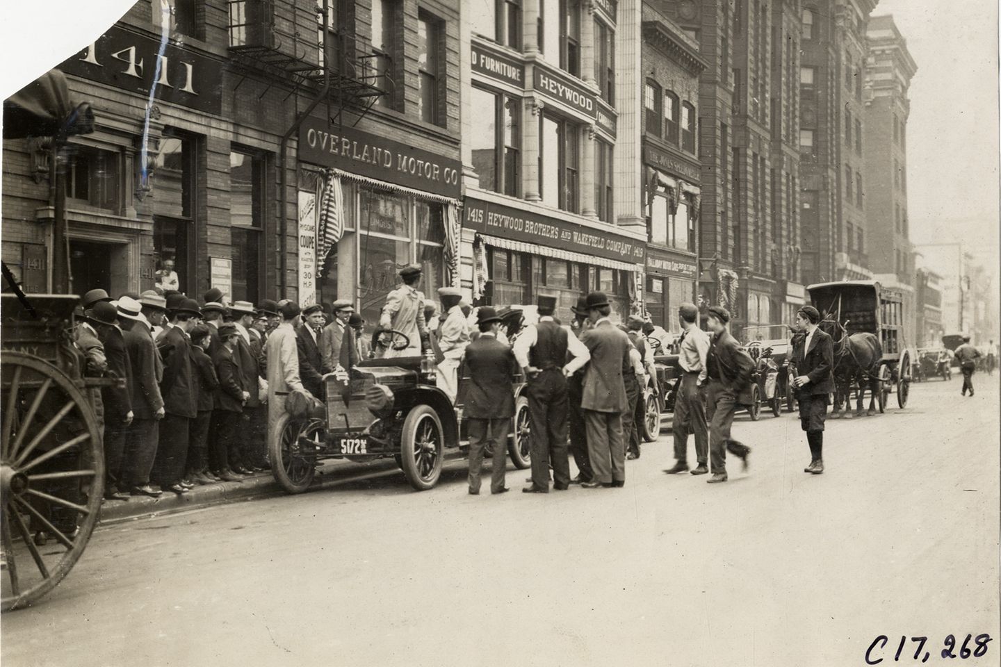 Eine Menschentraube vor einem parkenden Auto, in dem eine Frau steht und nach hinten schaut