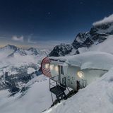 Eine futuristische Kapsel, die wie ein Raumschiff in der Stille der Alpen gelandet zu sein scheint: Am Rand des Abgrunds unter den eisigen Gipfeln der Grandes Jorasses ruht das Bivacco Gervasutti. Auf einem Felsvorsprung in 2.835 Metern Höhe trotzt die röhrenförmige Struktur den Kräften der Natur. Errichtet 2011 als Ersatz für eine alte Holzhütte, wurde das Biwak von einem italienischen Architekturbüro entwickelt und in Einzelteilen per Helikopter hierhergebracht. Innen erwartet Bergsteiger ein überraschend behaglicher Raum: warme holzverkleidete Kojen, solarbetriebene Beleuchtung und ein Panoramafenster, das den Blick auf die Bergwelt des Aostatals öffnet.