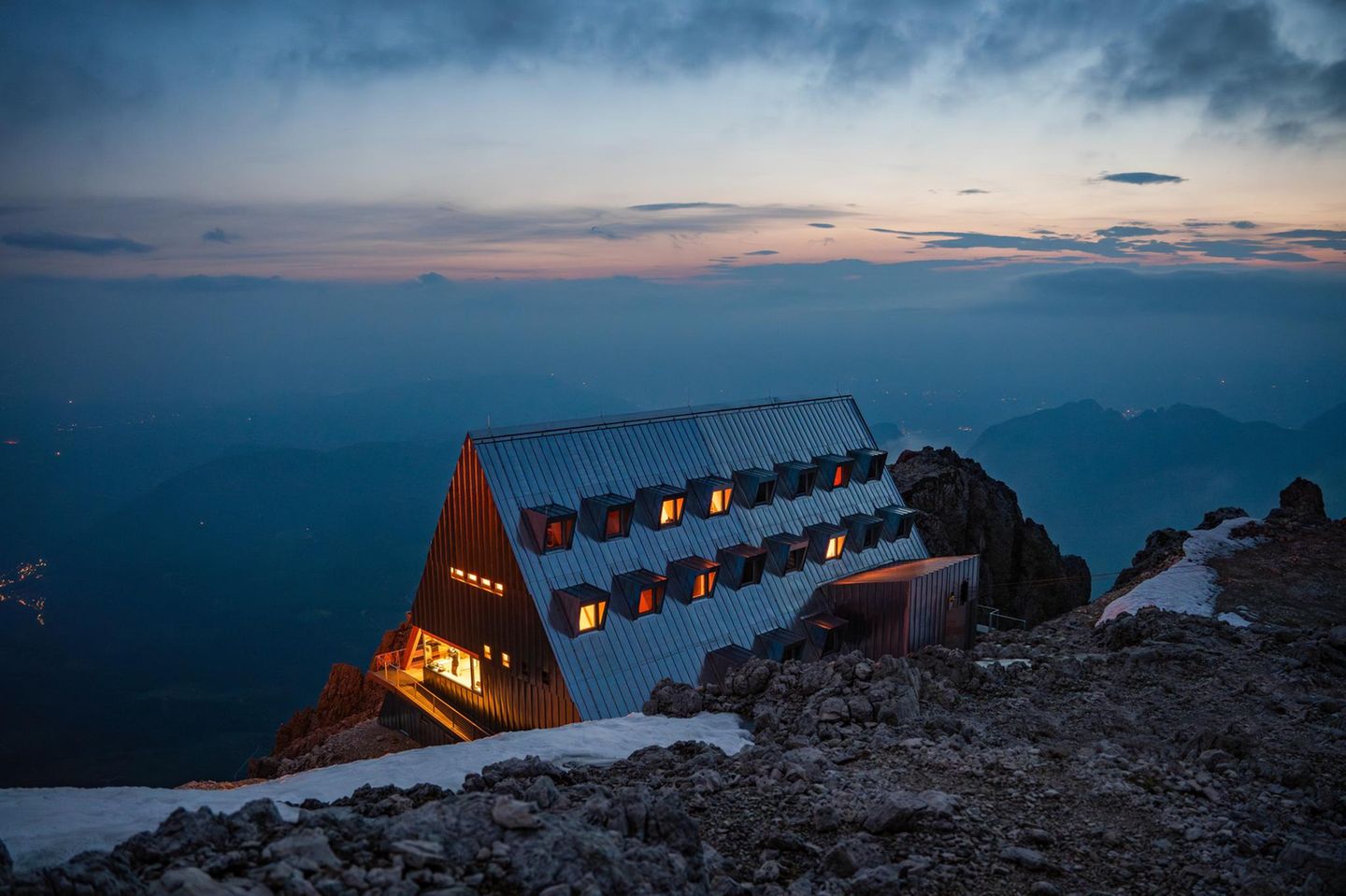 Rifugio Passo Santner in Bozen, Italien Auf 2.734 Metern thront diese klassische, aber modern gestaltete Hütte mitten im Naturpark Schlern-Rosengarten – und scheint mit einem warmen Leuchten zum Leben zu erwachen, sobald die Sonne hinter den Felstürmen der Rosengartengruppe versinkt. Das markante, dreieckige Gebäude schmiegt sich an den Stein und bietet einen unvergleichlichen Blick über Latemar, Ortler und bis zu den Alpen jenseits der Grenze. Einst erbaut vom Bergführer Giulio Gabrielli, verbindet das Rifugio Passo Santner mitten in den Dolomiten heute alpinistische Tradition und zeitloses Design.