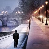 Eine Person läuft in der Dämmerung, bei Laternenlicht entlang eines Flusses in Paris