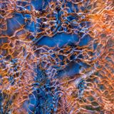 Komplexe Muster an einem Bergbach im Südtirol in blauer und orangener Farbe