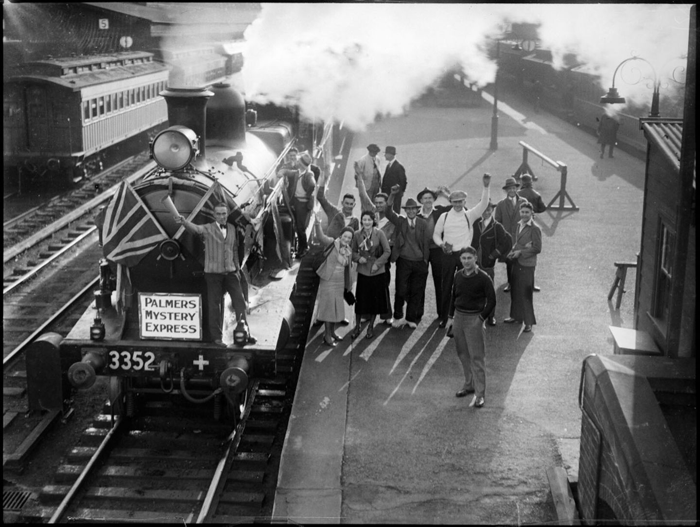 Menschen winken neben Dampflokomotive