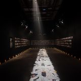 Langer, dunkler Raum, mit Bildern an den Wänden und Kerzen auf dem Boden