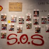 Ein Wand mit Fotografien der Geiseln in der Ausstellung, dazu die roten Buchstaben SOS