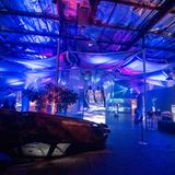 Blau beleuchete Ausstellungshalle mit beschädigtem Auto und Videoinstallationen