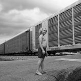 Ein Junge mit blonden Haaren streht barfuß auf einer Straße, während hinter ihm ein Zug vorbeifährt