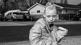 Ein Kind sitzt auf der Straße und hält ein Sandwich in der Hand