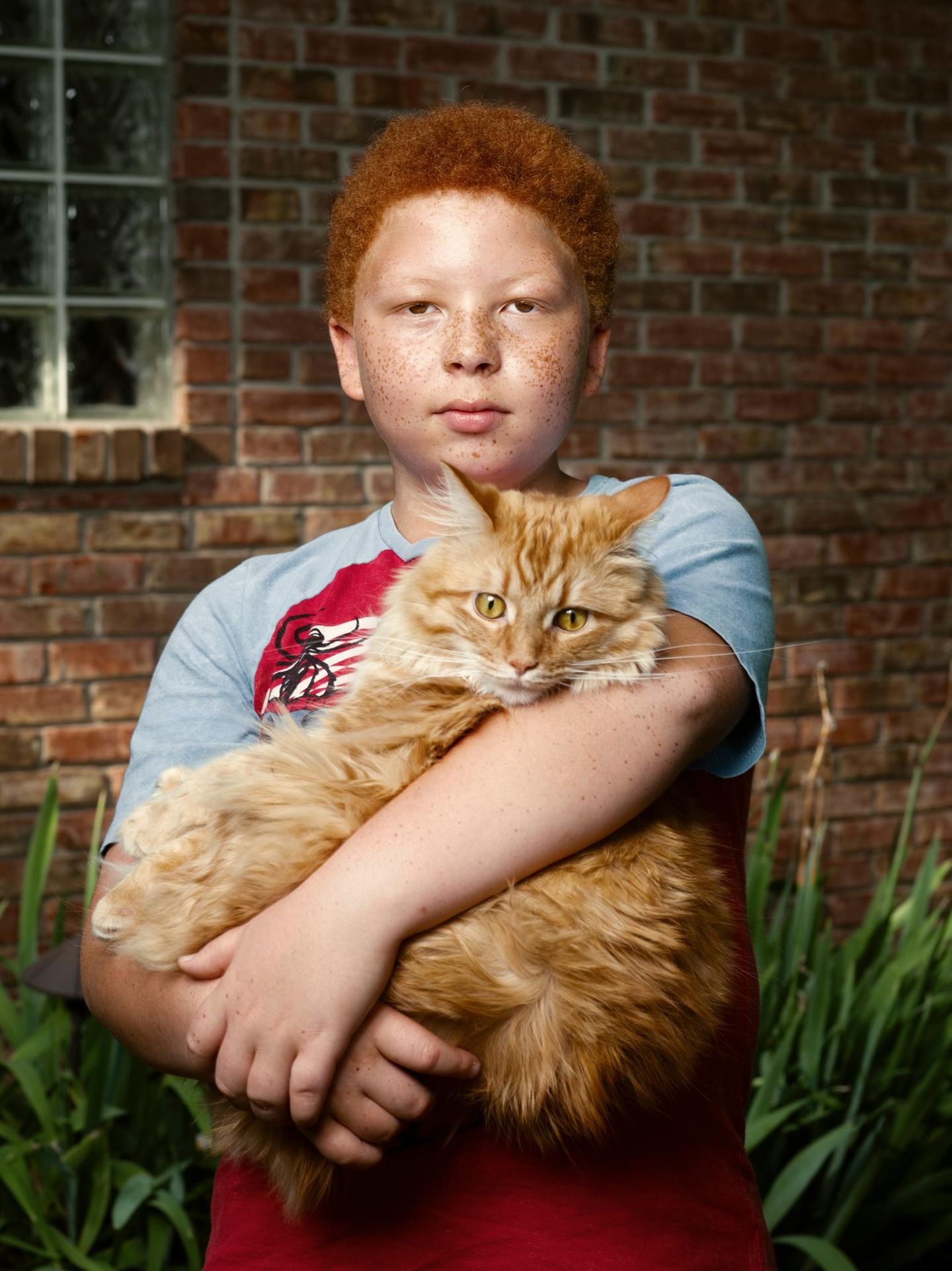 Alles ist möglich: Micah (10 Jahre) Ein Kind mit roten Haaren hält eine orangene Katze auf dem Arm