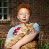 Ein Kind mit roten Haaren hält eine orangene Katze auf dem Arm