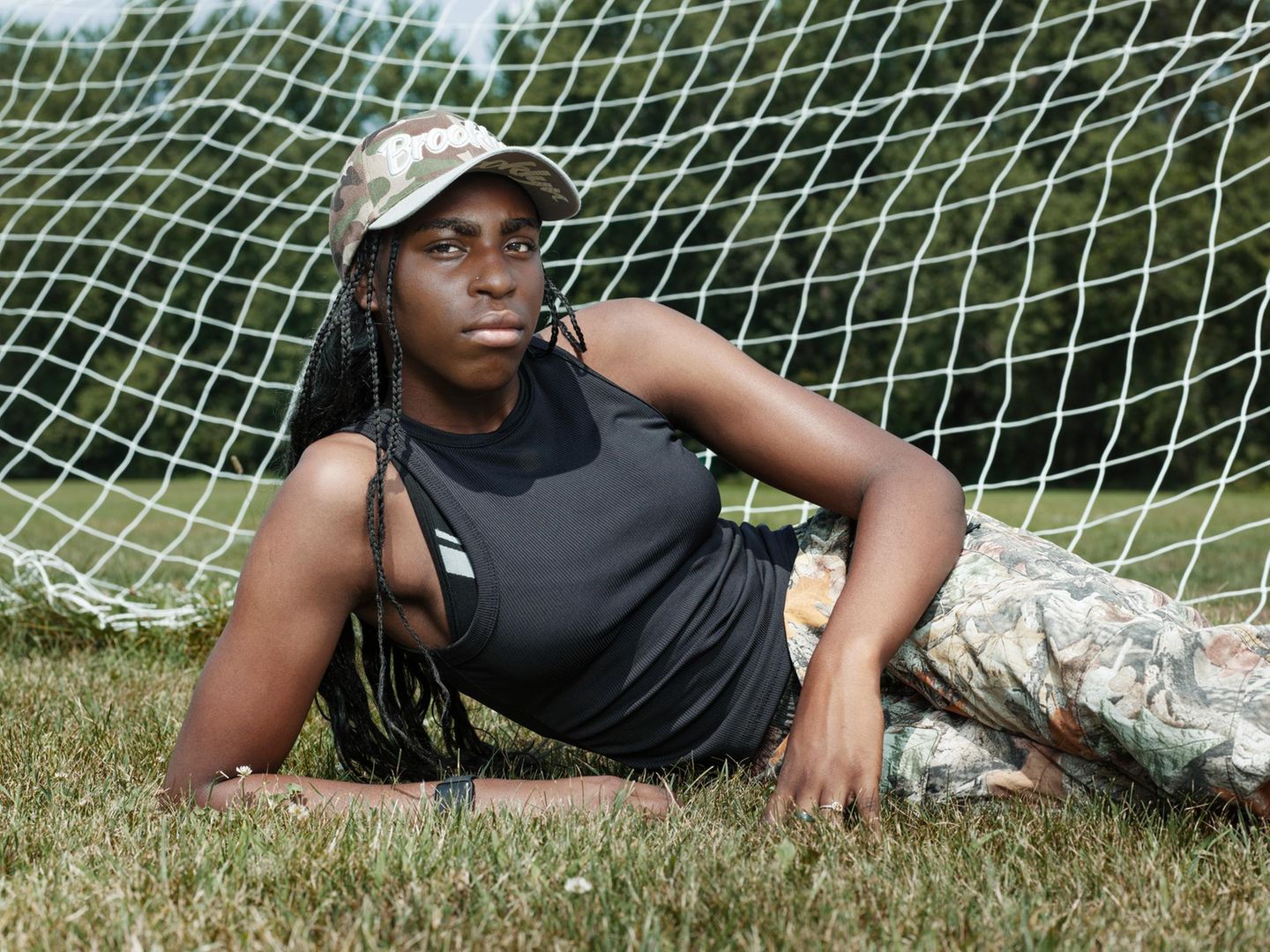 Laufen ist Freiheit: Crystal (16 Jahre) Eine Person mit einer Baseball-Cap liegt im Gras vor einem Fußballtor