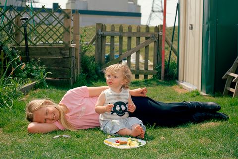 Ein Kind liegt im Garten, während ein Kleinkind vor ihr auf dem Rasen kniet. Vor ihnen ein Teller mit Essen