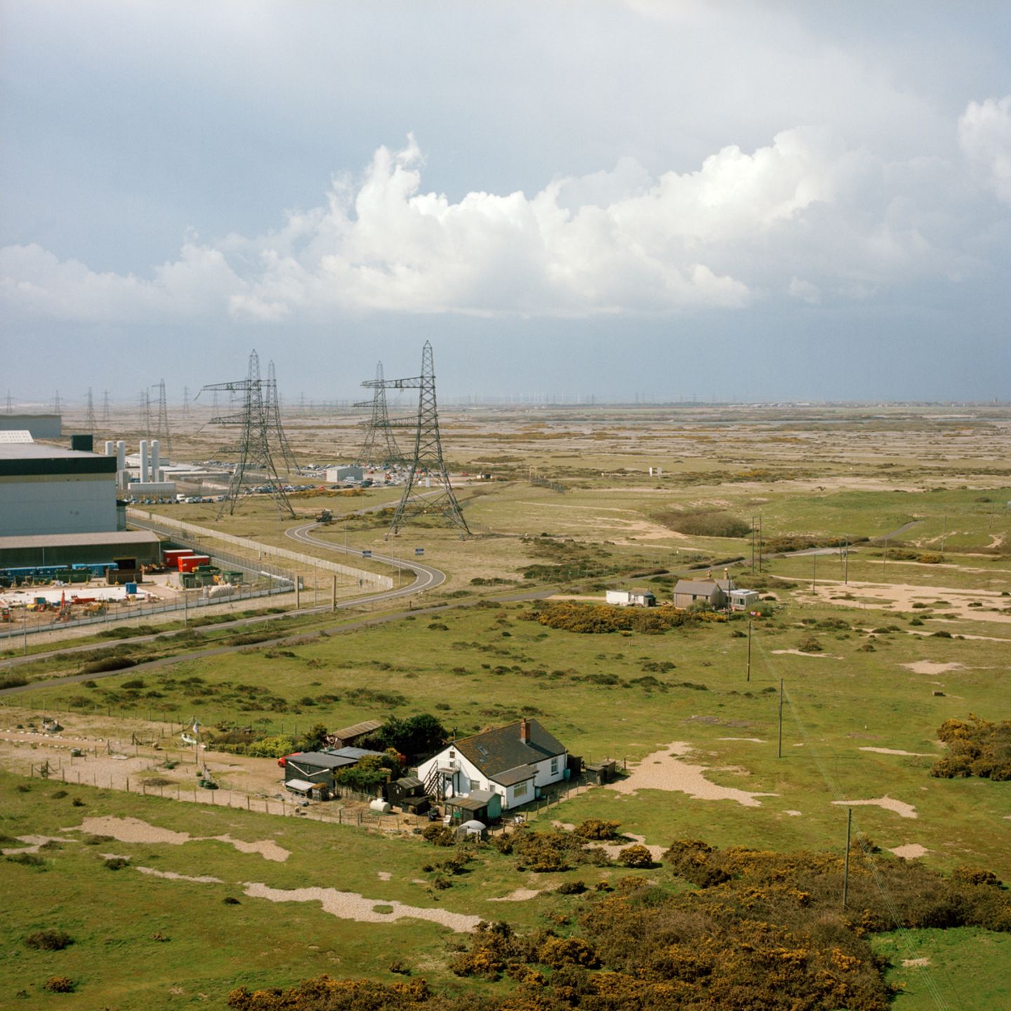 Eine Landschaft von oben, in der man grüne Wiesen sieht, ein Haus und in der Ferne Strommasten