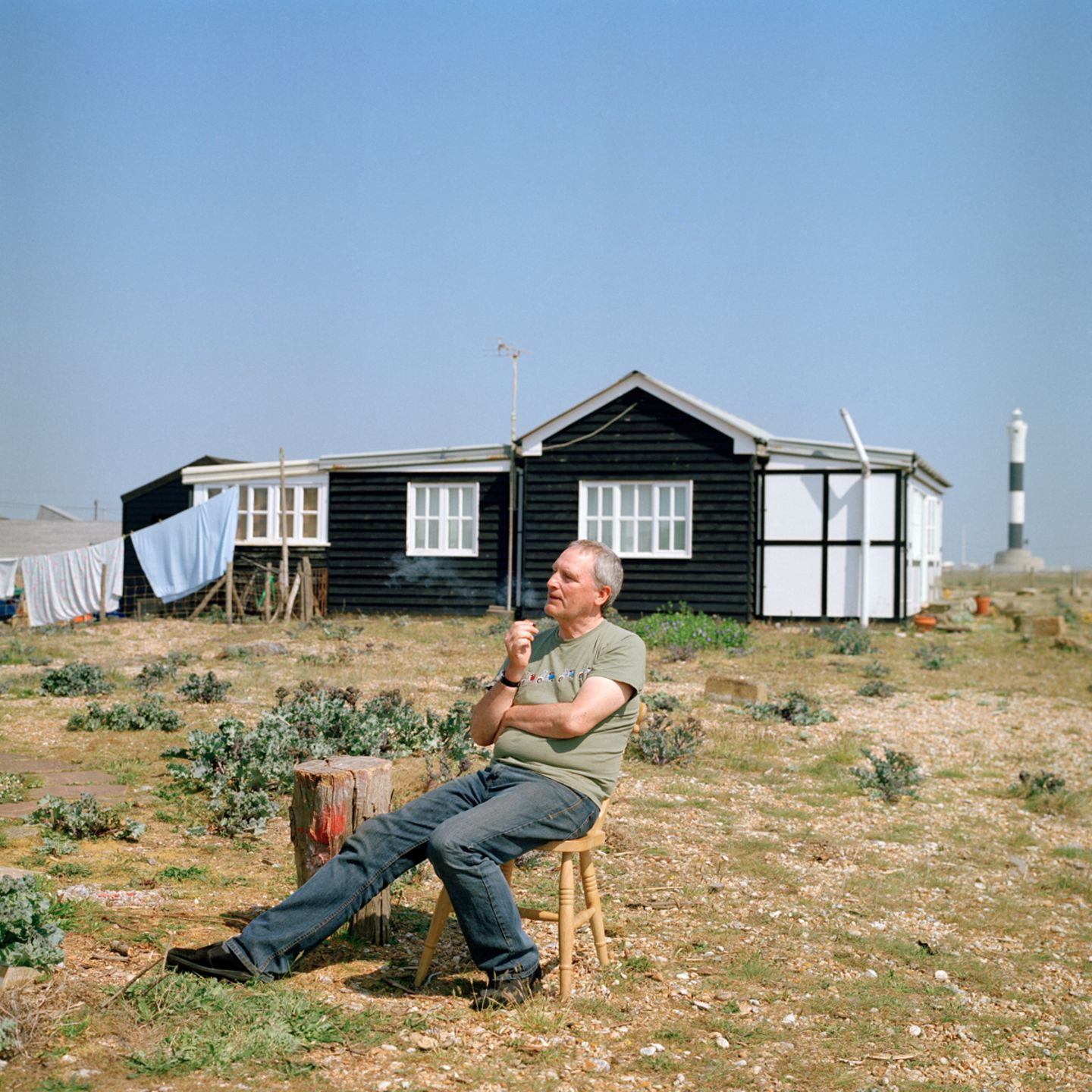 Eine Person sitzt entspannt auf einem Stuhl auf der Wiese, hinter ihr eine Holzhütte
