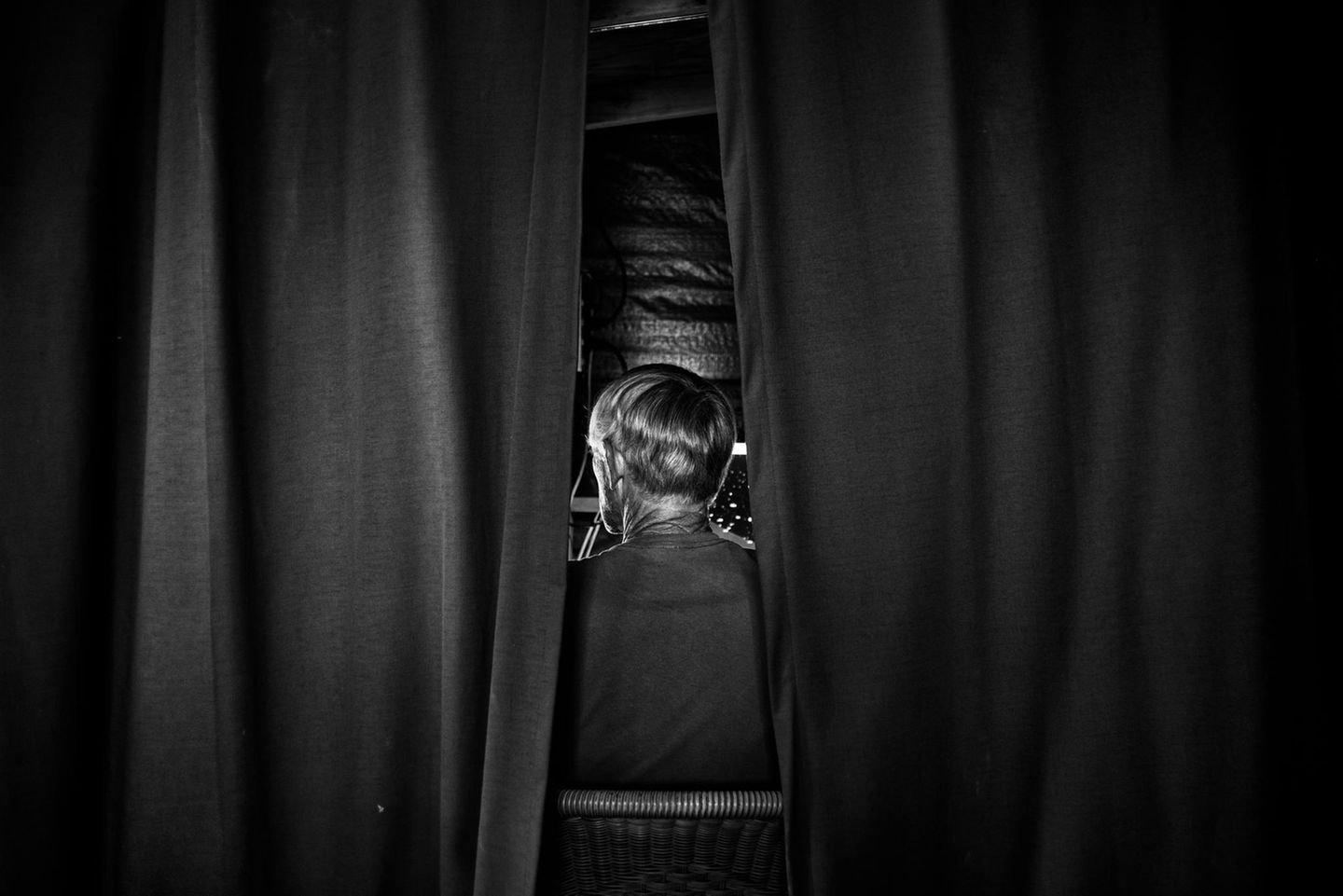 Eine Person von hinten, die zwischen Vorhängen sitzt