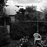 Ein Heimobservatorium in einem Garten in Australien. Im Vordergrund steht ein weißer Gartenstuhl