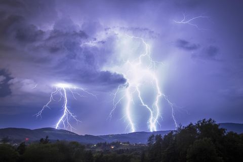 View of electrifying bolts of lightning illuminating the night sky above the rolling hills and trees in a display of raw power, Graz, Styria, Austria. 