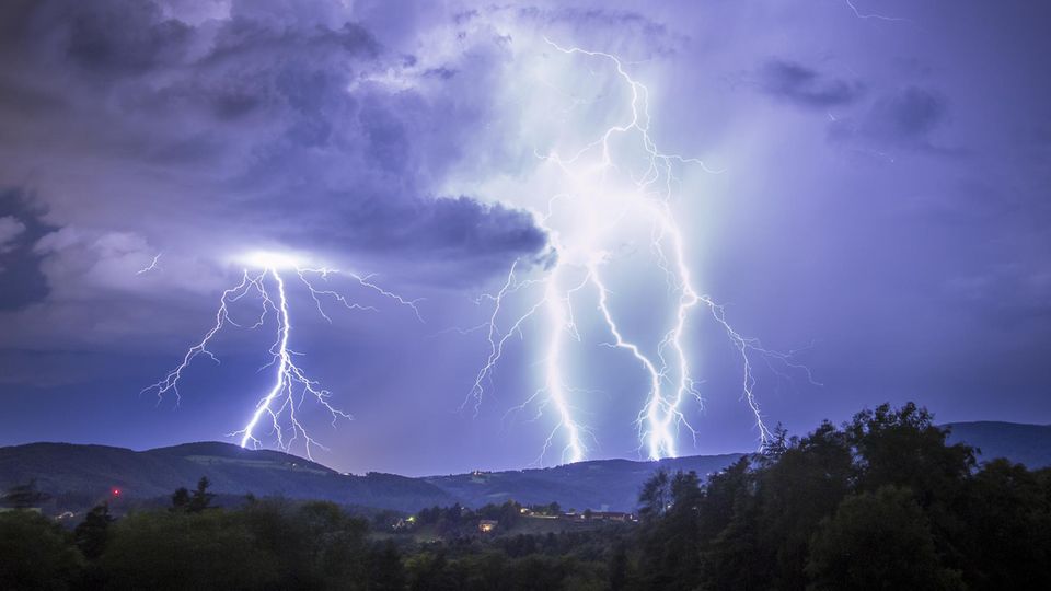 View of electrifying bolts of lightning illuminating the night sky above the rolling hills and trees in a display of raw power, Graz, Styria, Austria. 